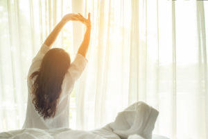 Photo of a woman stretching as she gets up from bed on a sunny morning. This photo represents how an anxiety therapist in California can help you cope with your anxiety and make you feel your best. Click here to learn more.