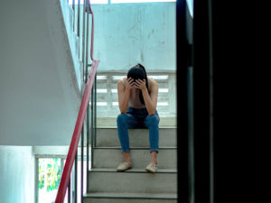 Photo of a woman sitting on the stairs with her head in her hands looking upset. This photo represents how anxiety symptoms can make you feel like you're struggling. Learn from an anxiety therapist in California how to cope with your anxiety.