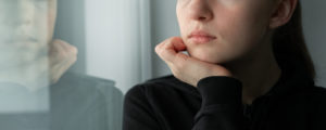 Photo of a woman looking out the window with her hand on her chin. This photo represent how unresolved trauma can affect your life. Learn from an online trauma therapist in San Ramon, CA how to manage.