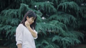 Photo of a woman standing outside looking down at the ground with her hand on her face. This photo represents how unresolved trauma can affect your life. Learn from an online trauma therapist in San Ramon, CA how to manage.