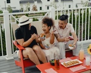 Photo of a family sitting on a porch outside smiling and eating. Struggling with communication in your family? Learn how family counseling in San Ramon, CA can help you learn better communication skills.