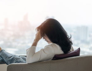 Photo of a woman sitting on a couch looking anxious with her hand on her forehead. This photo represents how brainspotting therapy in California can help you overcome your anxiety symptoms and live a happier life.