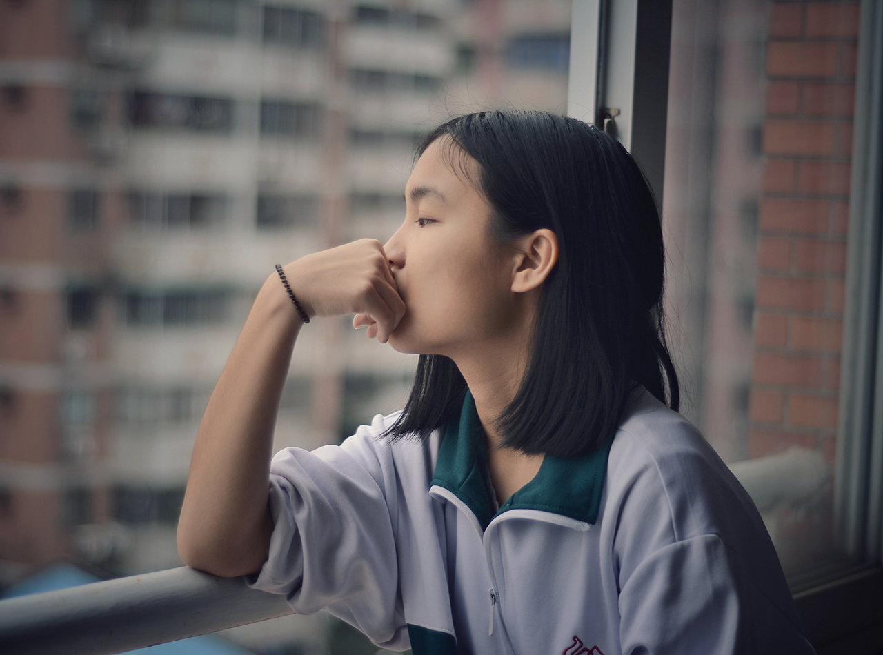 A woman looks out a window with her hand against her mouth. This could represent the isolation a trauma therapist in San Ramon, CA can help you overcome. Learn more about brainspotting therapy in San Ramon, CA and other services today by contacting a brainspotting therapist in San Ramon, CA.