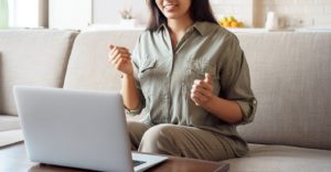 Photo of a woman sitting on a couch happpily using a laptop to access online anxiety therapy in San Ramon, CA to help manage her anxiety symptoms.