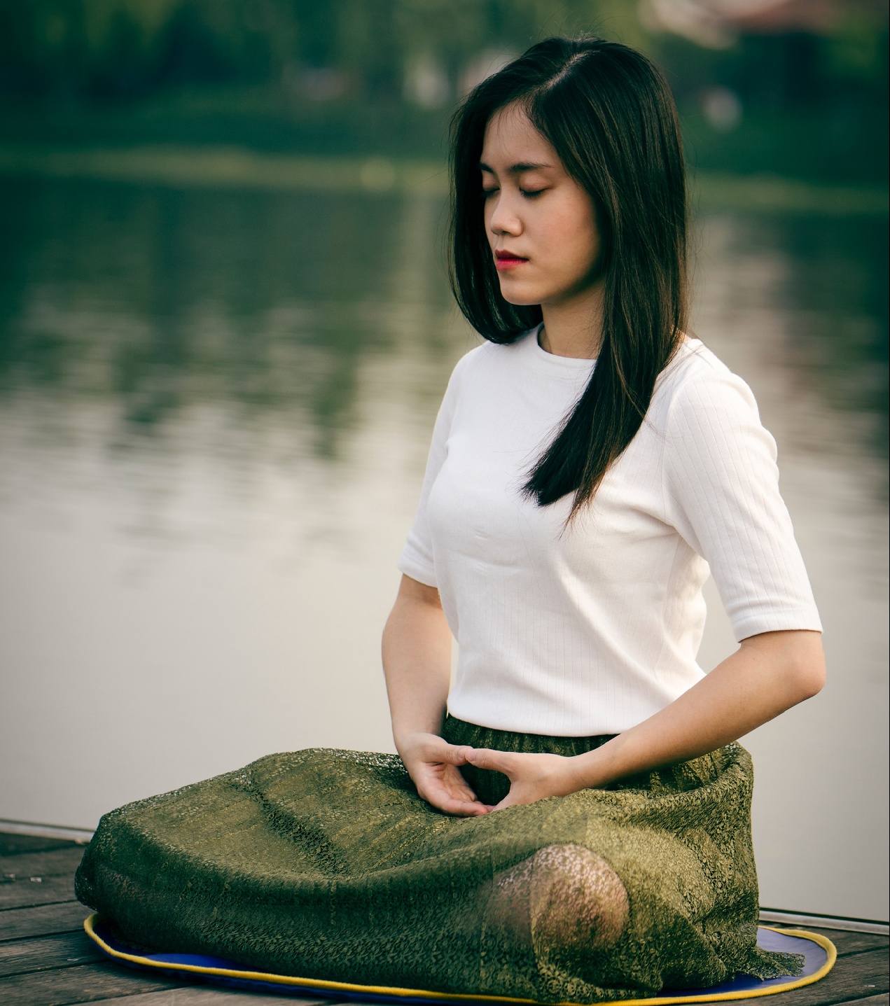 Photo of an Asian American woman sitting beside water practicing meditation. This photo represents how coping skills such as meditation can be learned with anxiety therapy in San Ramon, CA.