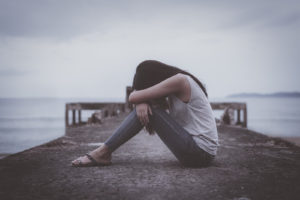 Photo of an upset woman sitting on a pier with her head on her knees. Discover how a trauma therapist in San Ramon, CA can help you overcome your unresolved trauma.