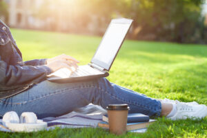 Photo of a woman sitting on the grass on a sunny day using a laptop to access therapy online. Begin working with an online trauma therapist in San Ramon, CA to start your healing journey.