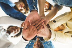 A group of people stack their hands on one another as they smile at the camera. This represents the support offered by an online trauma therapist in San Ramon, CA. Learn more about trauma therapy in San Ramon, CA for more info. 