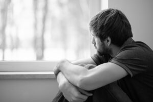 A man with a bleak expression looks out the window. This could represent the pain a trauma therapist in San Ramon, CA can offer today. Learn more about online trauma therapy in California and other services an online trauma therapist can offer. 
