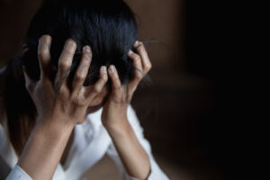 A close up of a woman holding her head in her hands in a dark room. This could represent the isolation of anxiety that online anxiety therapy in San Ramon, CA can support. Learn more about anxiety treatment in San Ramon, CA by ctonacting an anxiety therapist in San Ramon, CA today. 