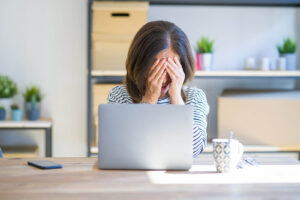 A woman covers her face while sitting in front of a laptop. This could represent the stress of perfectionism that a brainspotting therapist in San Ramon, CA can help you overcome. Learn more about anxiety therapy in San Ramon, CA by searching for brainspotting in California today. 